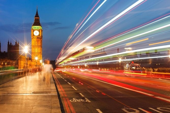 Big Ben at night above a road turned into streaks of red and white light by passing buses and taxis