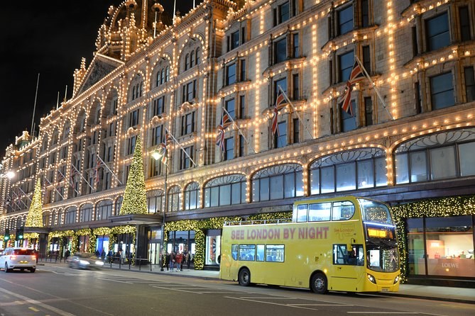 The front of Harrods outlined in thousands of lights at night, the open-top bus passing along Brompton Road