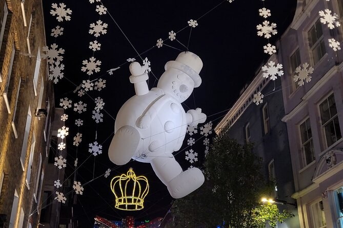 A large illuminated snowman and white snowflake lights hanging above a Mayfair street at night