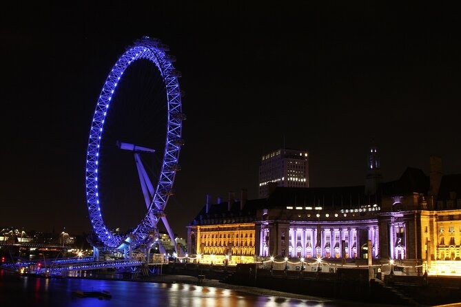 The London Eye lit blue at night above the floodlit front of County Hall