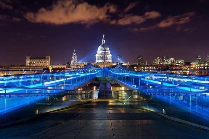 The Millennium Bridge lit electric blue along its length at night, part of the Illuminated River scheme, with St Paul's beyond