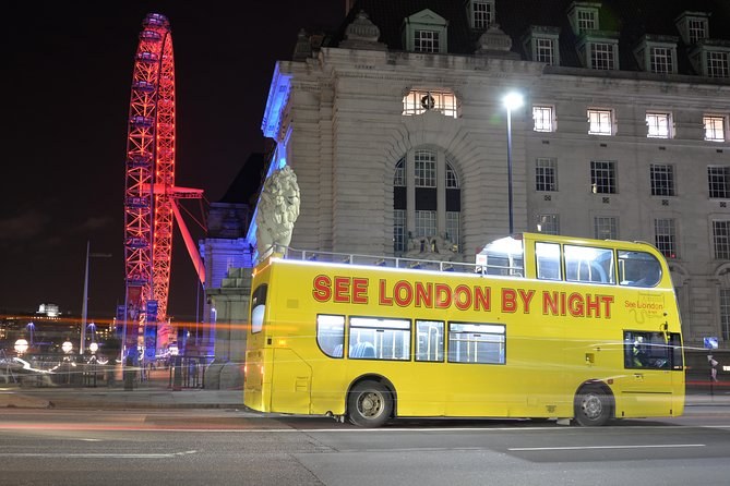 The open-top night sightseeing bus at a stop with the London Eye lit red behind it