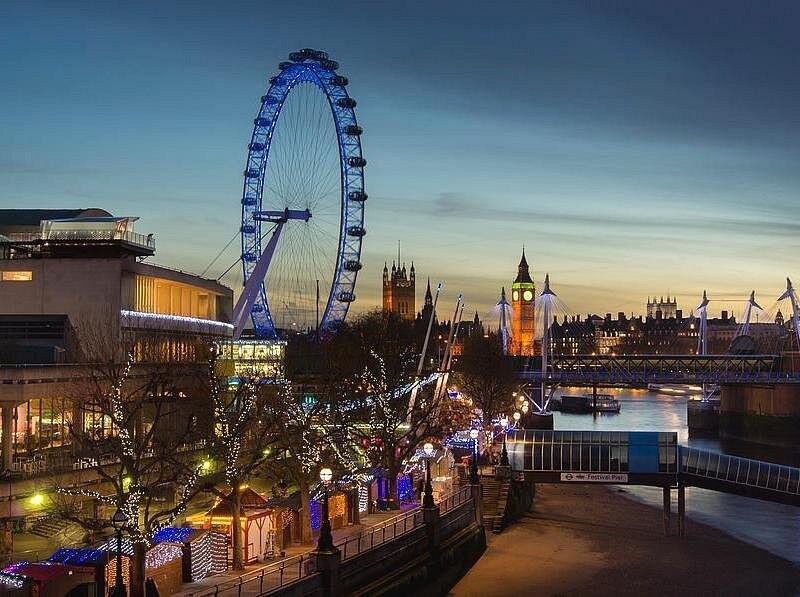 The South Bank at dusk with the London Eye, Big Ben and the lit stalls of a riverside Christmas market along the water