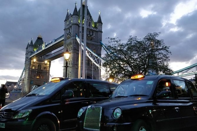 Two London black cabs parked on the cobbles below Tower Bridge as the light goes, the bridge lit blue behind them